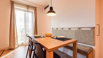 A dining area with a wooden table, black chairs, a bowl, and glasses. There is a bench with a striped cushion against a wall with a radiator.