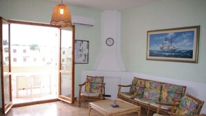 A living room with a sofa, chairs, a coffee table, and a painting of a ship on the wall. - Casa Calamaro (Alghero)
