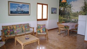 A room with a sofa, chairs, a table, and a refrigerator. - Casa Calamaro (Alghero)