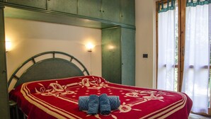 A bed with a red and white patterned bedspread, a green metal headboard, and two rolled-up towels on the bed. - Casa Cernia (Alghero)