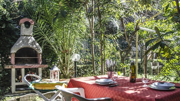 An outdoor dining area with a red tablecloth, a pizza oven, and a lantern. - Casa Cernia (Alghero)