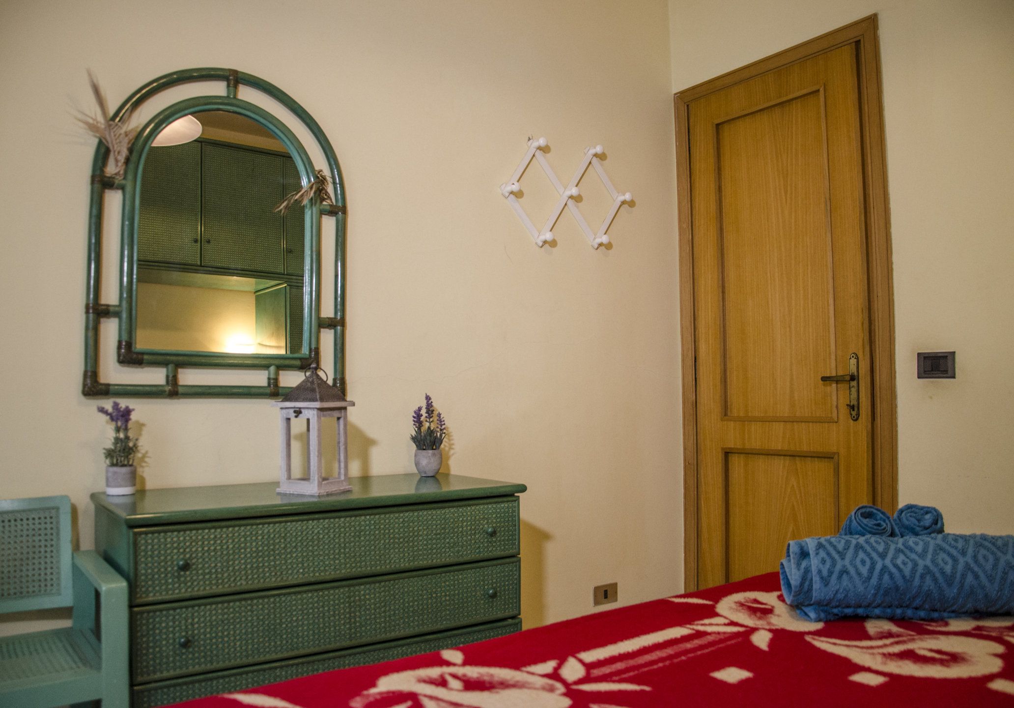 Una habitación con un aparador verde, un espejo, una puerta de madera y una cama con colcha de rayas rojas y blancas.