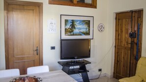 A room with a wooden door, a television mounted on a stand, a dining table with a bowl, and a yellow chair. - Casa Cernia (Alghero)