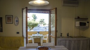 A dining area with a table, chairs, a bowl, a yellow sofa, and a view of the street through an open door. - Casa Cernia (Alghero)