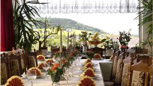 A dining table set with plates, glasses, and flowers, with a view of a landscape. - Gästehaus Hutweide (Baerenstein)