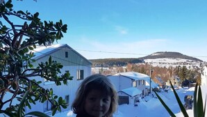 A child standing indoors with a view of a snowy landscape and buildings in the background. - Gästehaus Hutweide (Baerenstein)