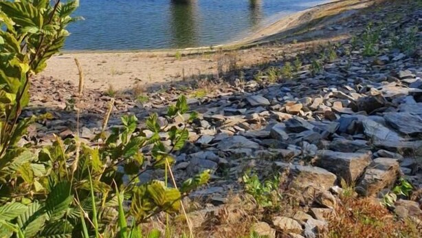 A stone tower by a calm lake with a wooden bridge. - Gästehaus Hutweide (Baerenstein)