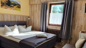 A bedroom with a bed, a window with curtains, a radiator, and a painting on the wall. - Gästehaus Hutweide (Baerenstein)