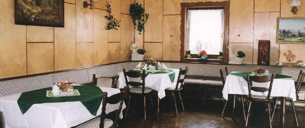Un espace repas avec des murs lambrissés en bois, des nappes vertes et des nappes blanches.