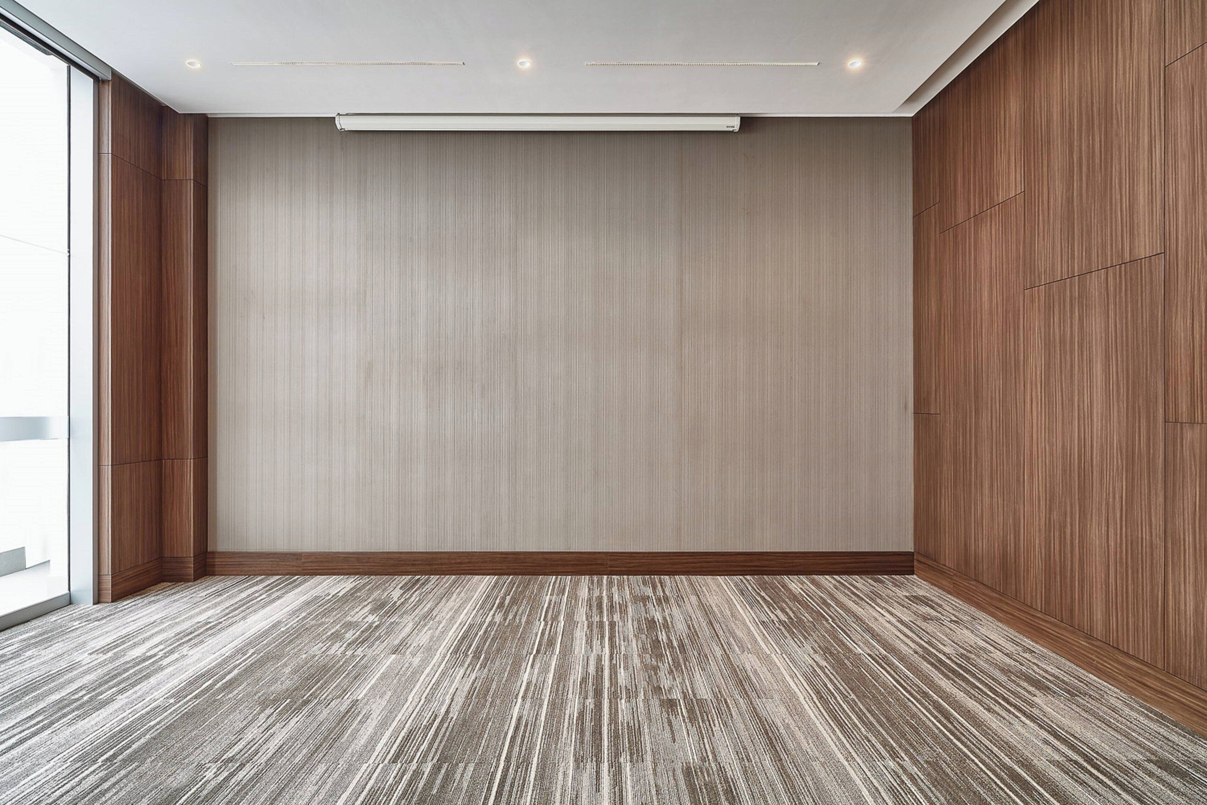 A room with a wooden floor, a large window, and a wall with vertical lines.