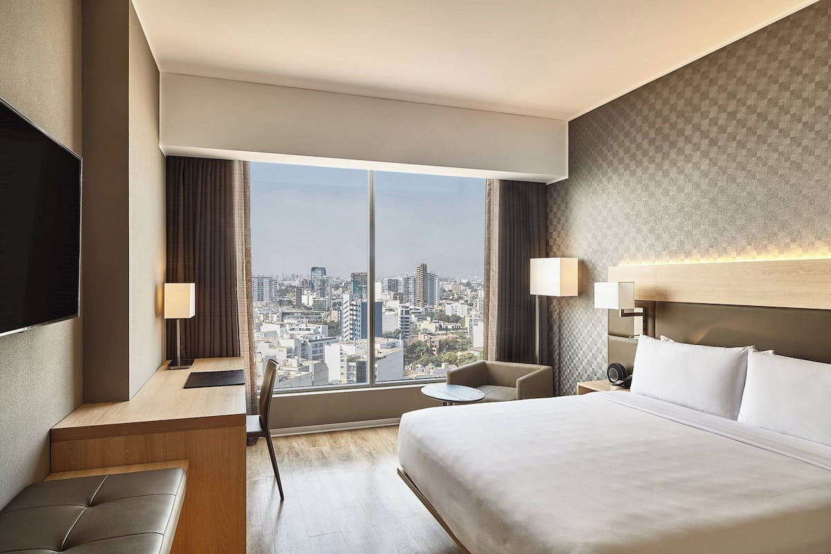 Une chambre d’hôtel avec un grand lit, un bureau, une chaise, une télévision et une vue sur la ville.