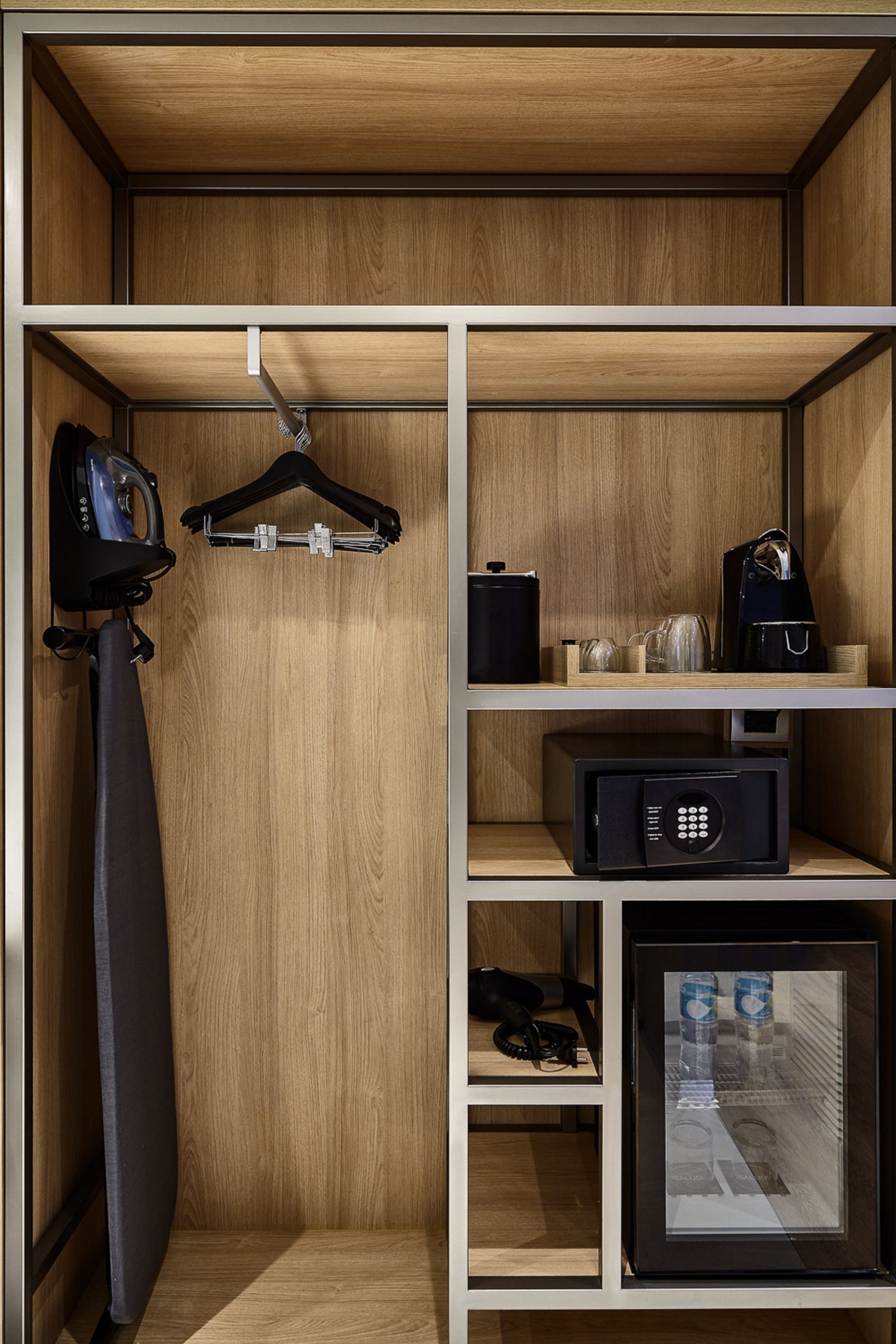 Habitación de hotel con un armario de madera, una plancha, una caja fuerte y un refrigerador pequeño.
