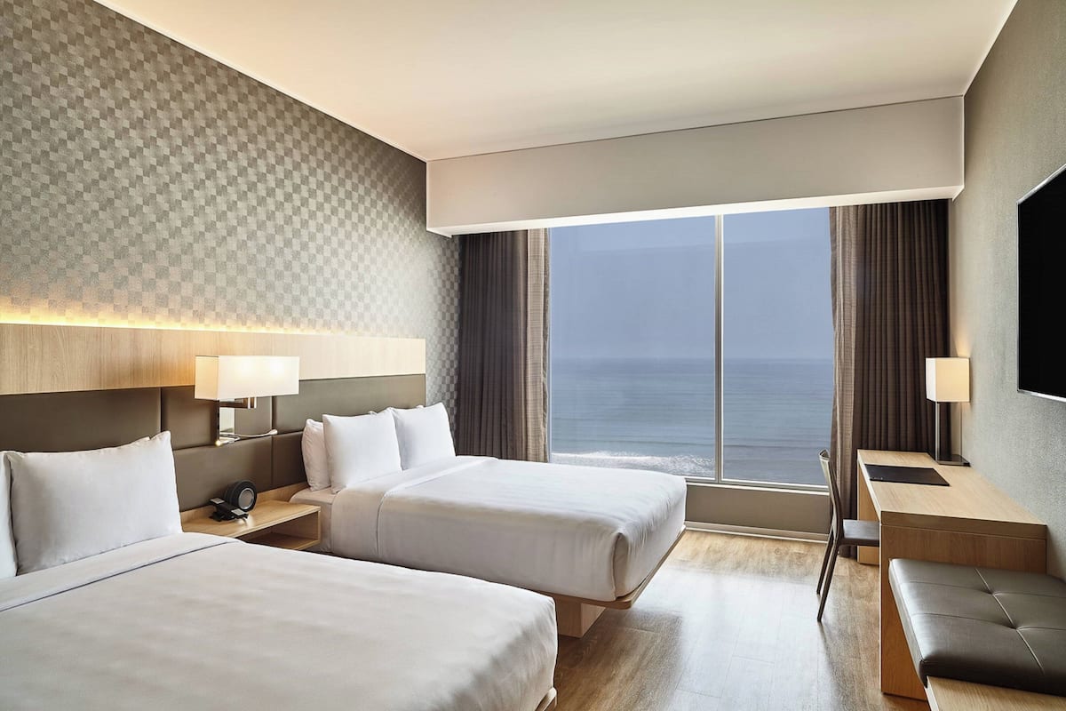 Une chambre d’hôtel avec deux lits, un bureau, une chaise, une télévision et une vue sur l’océan.