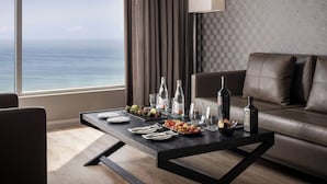 Una habitación de hotel moderna con un sofá de cuero, una mesa de comedor con platos, vasos y botellas, y vista al océano.