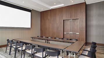 A conference room with a long table, multiple chairs, a projector screen, and a wooden panel wall.