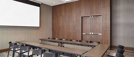 Une salle de conférence avec une longue table, de nombreuses chaises, un écran de projection et un mur recouvert de panneaux en bois.