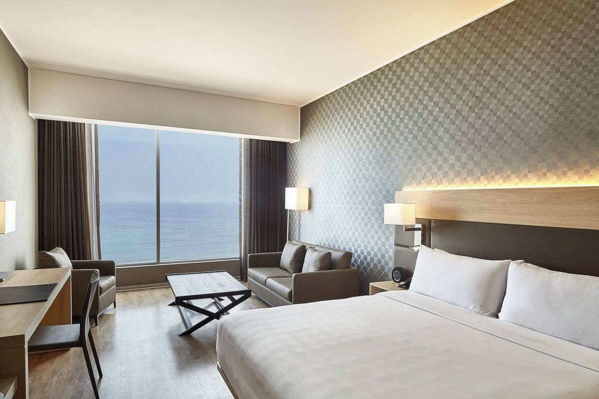 Une chambre d’hôtel avec un grand lit, un bureau, une chaise, un canapé et une vue sur l’océan.