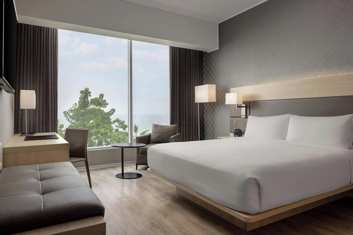 Une chambre d’hôtel moderne, dotée d’un grand lit, d’un bureau, d’une chaise et offrant une vue sur l’extérieur.