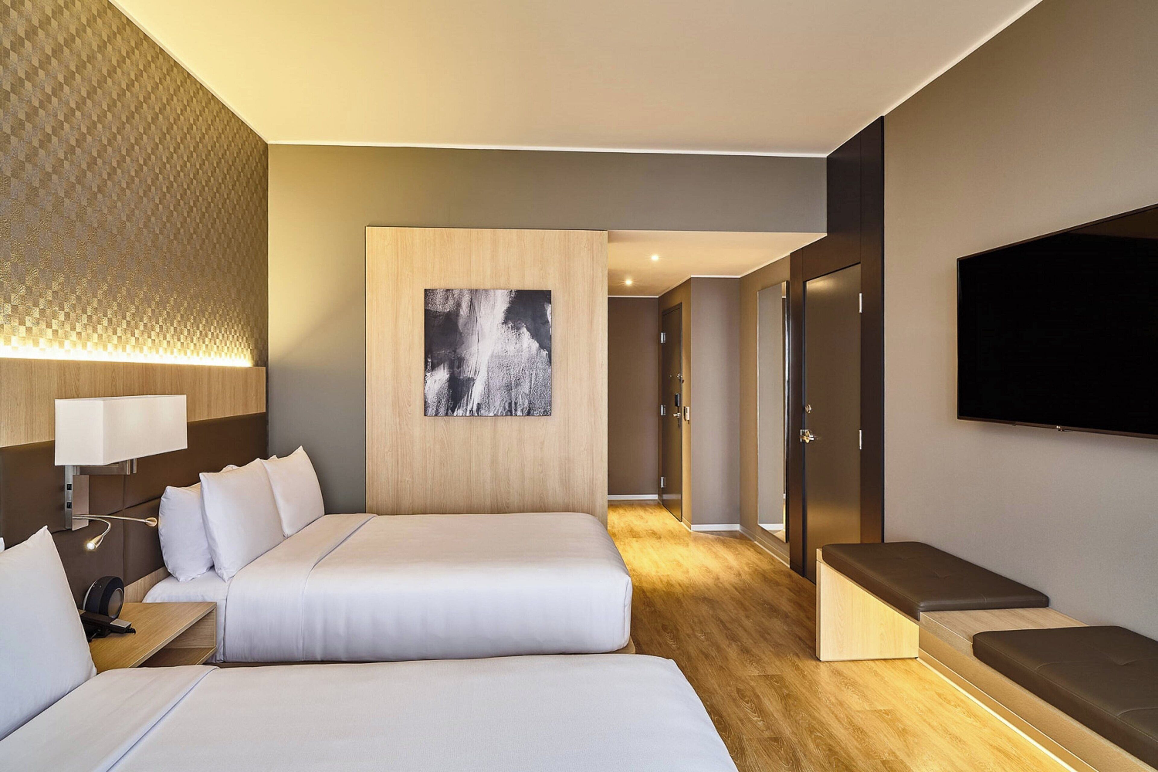 A hotel room with two beds, a flat-screen TV, a painting, and a wooden floor.