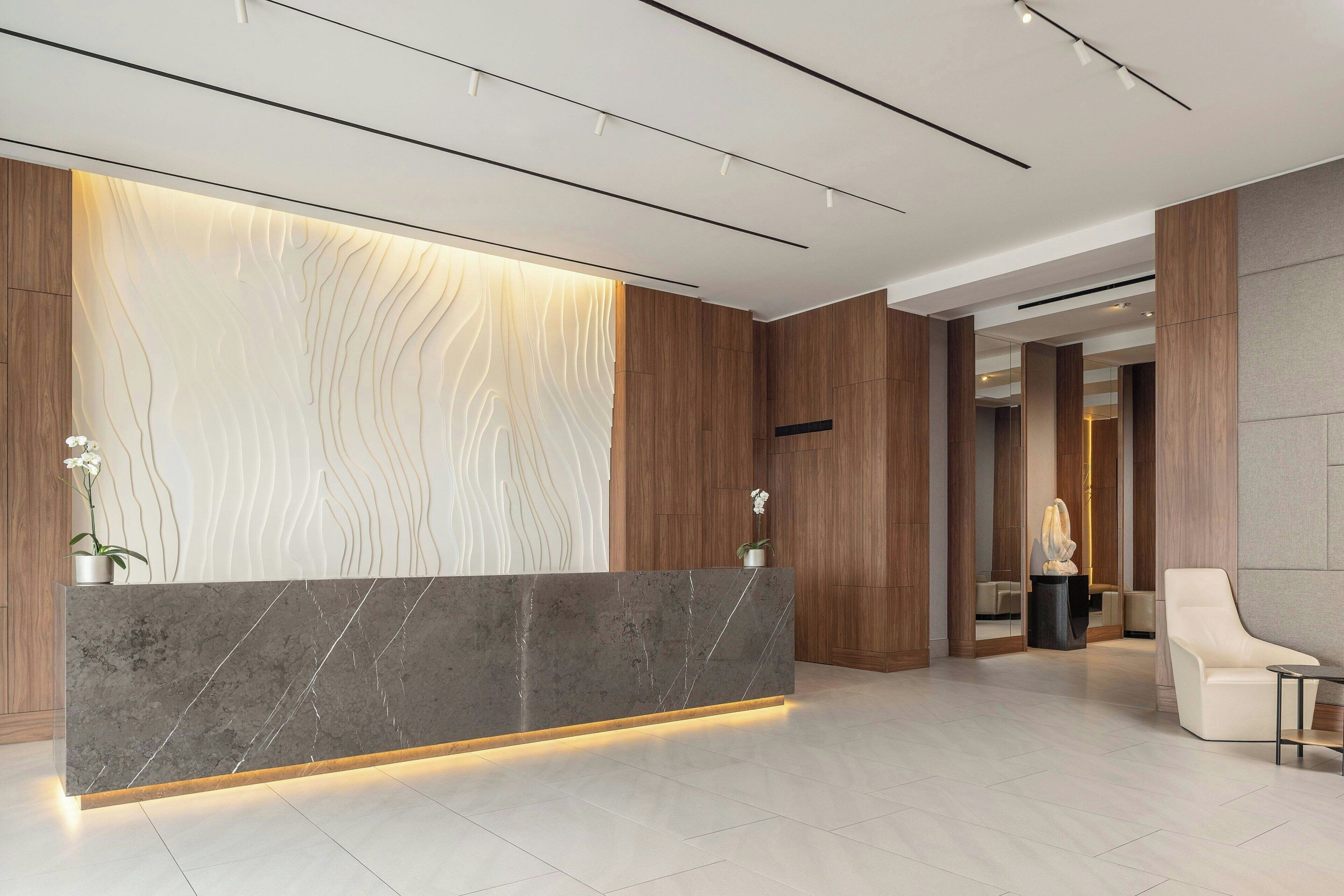 A modern reception area with a marble reception desk, wooden paneling, and a minimalist design.