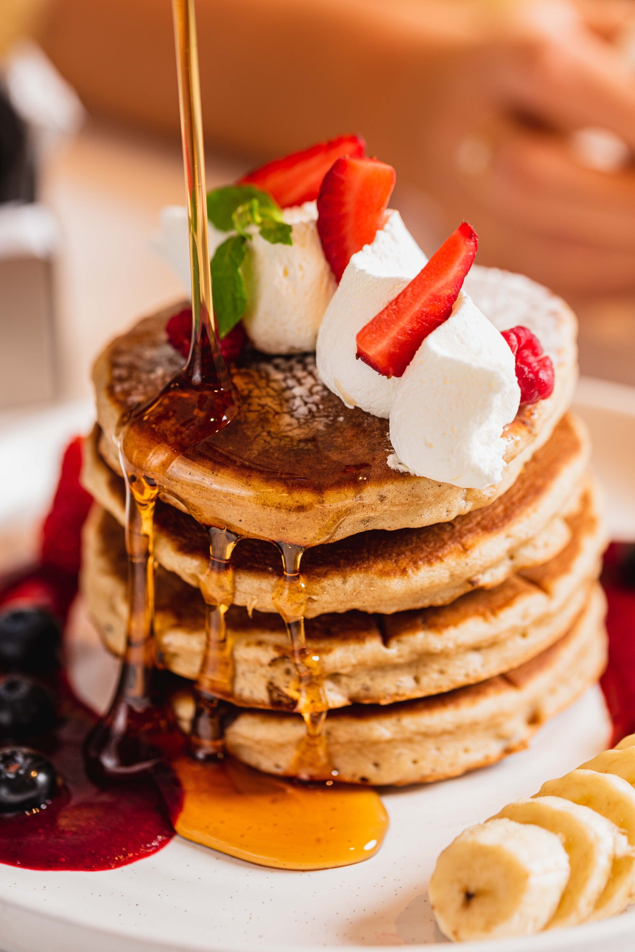 Una pila de tortitas con jarabe, fresas, frambuesas y crema batida.