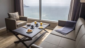 Una habitación moderna con un ventanal grande con vistas al mar, una mesa de comedor preparada para el desayuno y dos sofás.