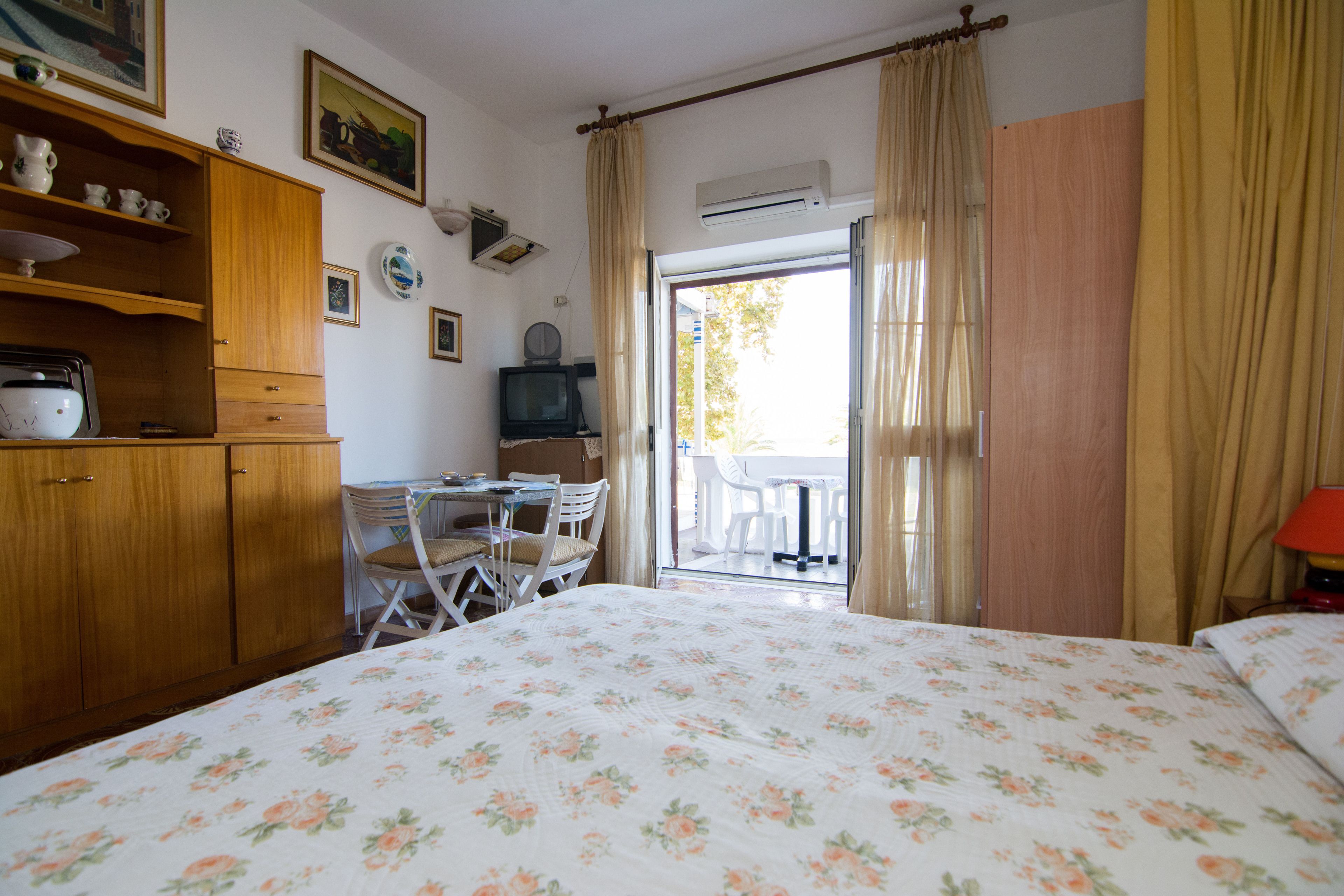 A bedroom with a bed, a wooden cabinet, a television, and a dining area with chairs and a table.