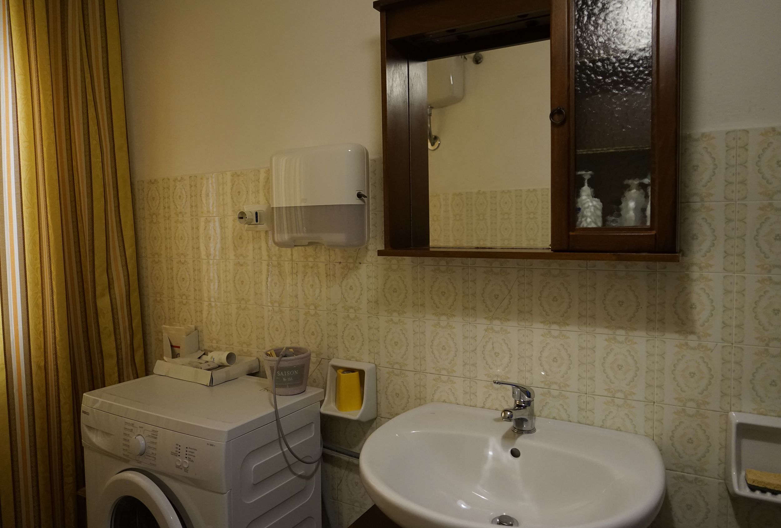 A bathroom with a washing machine, sink, mirror, and patterned tiles.