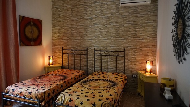Una habitación con dos camas individuales, una pared de ladrillo, un aire acondicionado y una obra de arte colgada en la pared.