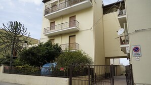 Un edificio residencial de varios pisos con balcones, entrada protegida por un portón y un cartel que indica prohibido estacionar.
