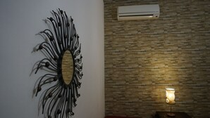 Una habitación con un espejo en la pared, un muro texturizado, un equipo de aire acondicionado y una lámpara de mesa.