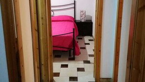 A narrow hallway leading to a bedroom with a bed, a nightstand, and a wall-mounted air conditioning unit. - Casa Barchetta (Alghero)