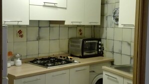 A compact kitchen with white cabinets, a gas stove, a toaster, and a washing machine. - Casa Barchetta (Alghero)