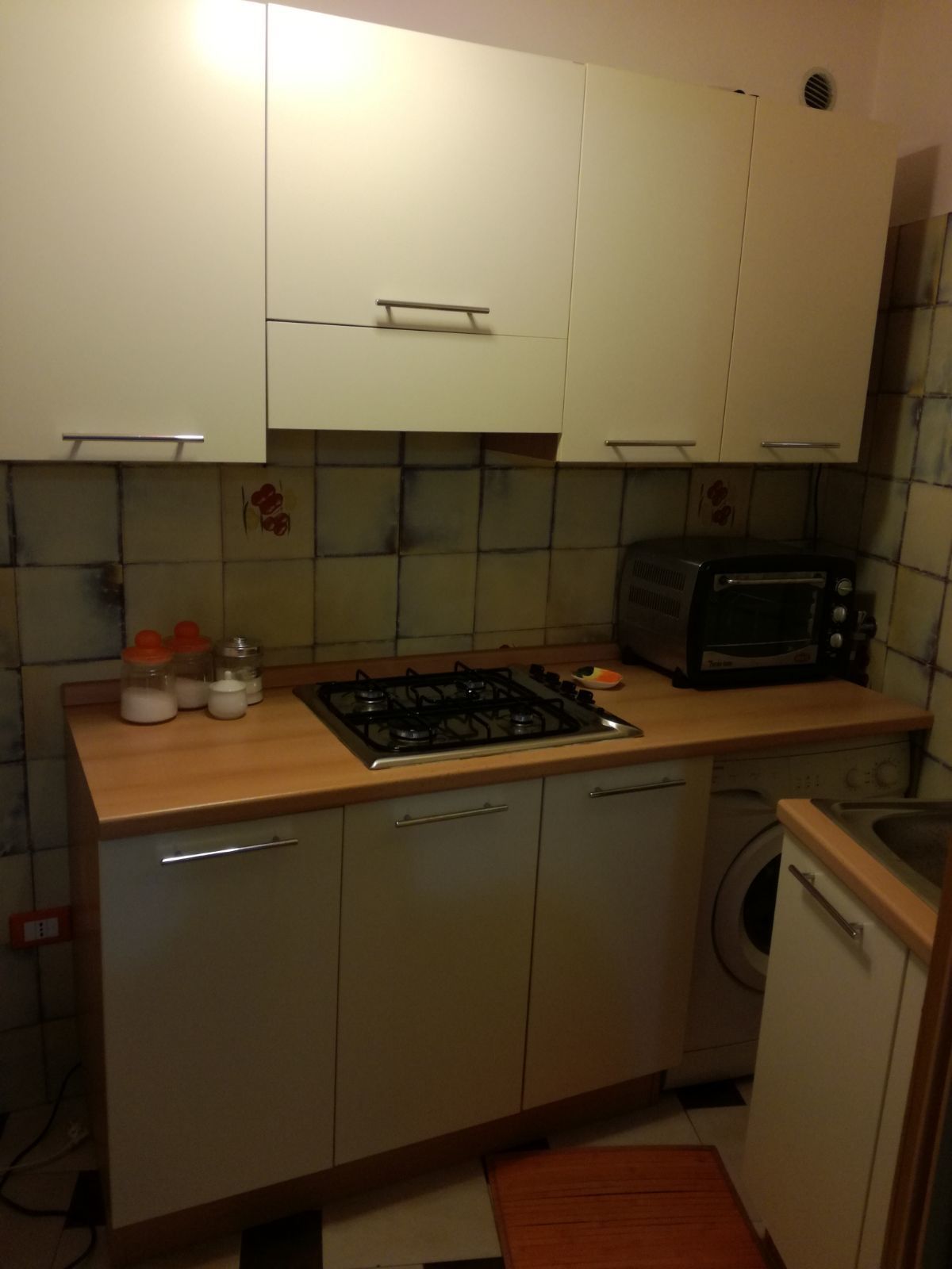 Cocina compacta con estufa a gas, microondas y lavadora. Cuenta con armarios con manijas y salpicadero de azulejos.
