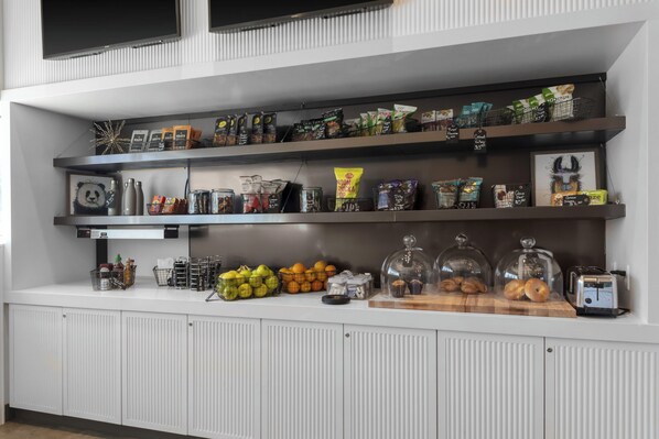 A well-organized kitchen area with multiple shelves stocked with snacks, fruits, and condiments. - Aloft by Marriott Glendale at Westgate (Glendale)