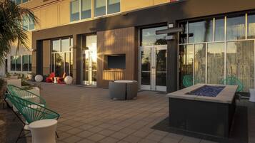 Un espacio exterior con mobiliario moderno, una chimenea y un edificio con ventanas amplias y techo plano.