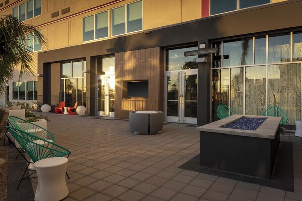 An outdoor patio area with modern seating, a fire pit, and a building with large windows and a flat roof. - Aloft by Marriott Glendale at Westgate (Glendale)