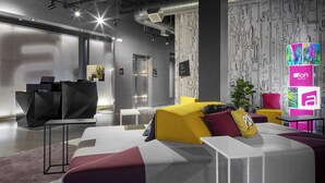 A modern hotel lobby with a sectional sofa, a reception desk, and a digital display. - Aloft by Marriott Glendale at Westgate (Glendale)