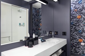 Une salle de bain moderne avec un grand miroir, un lavabo blanc et une douche.