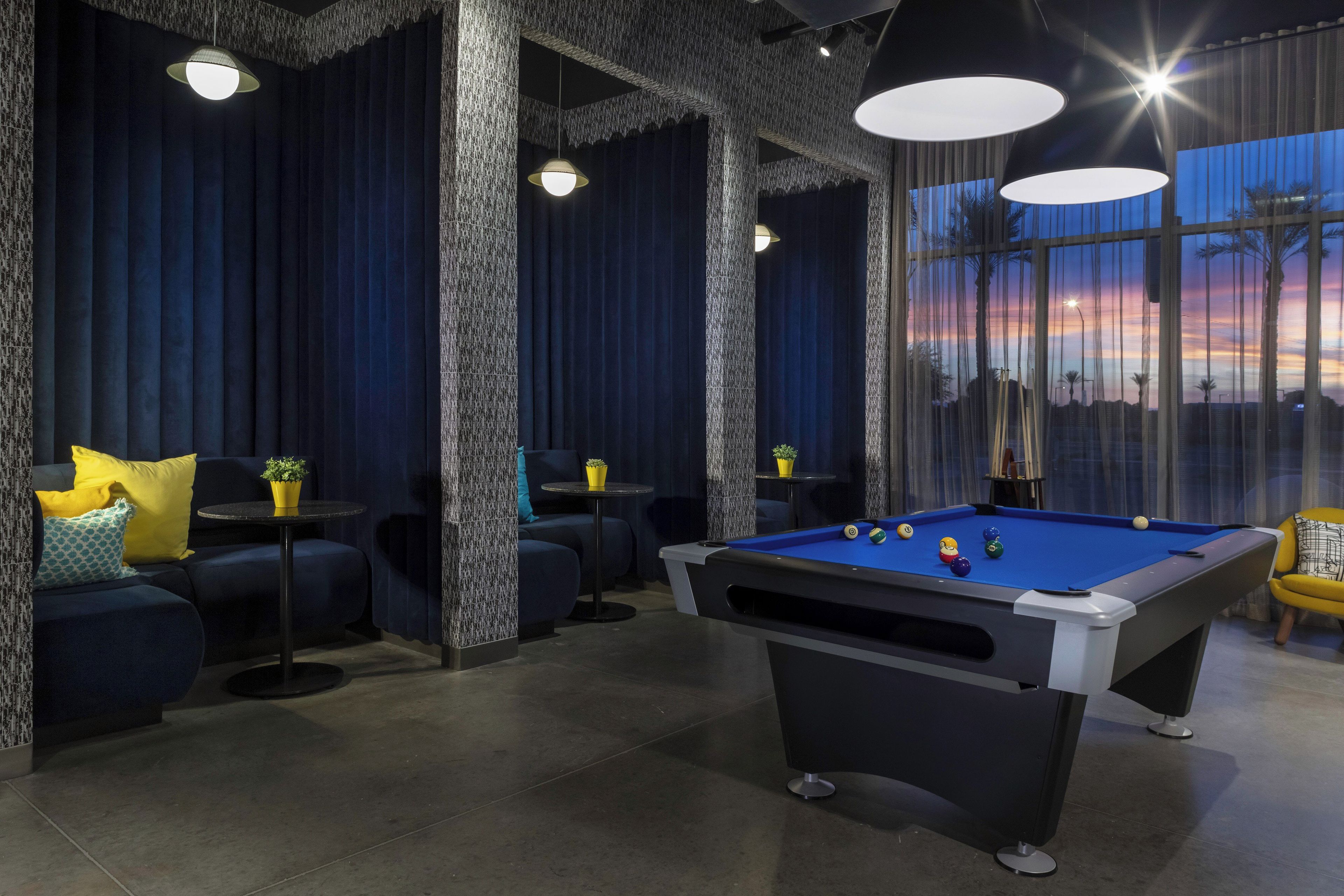 A pool table in a room with dark blue curtains, a sofa with cushions, and a table with a potted plant.