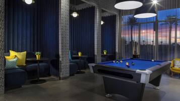 A pool table in a room with dark blue curtains, a sofa with cushions, and a table with a potted plant.