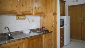 A kitchen with wooden cabinets, a stainless steel sink, a stove, and a microwave. - Casa Mostella (Alghero)