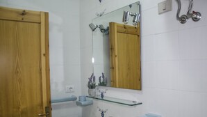 A bathroom with a wooden door, a white sink with a mirror above it, and a shower with a chrome fixture. - Casa Mostella (Alghero)
