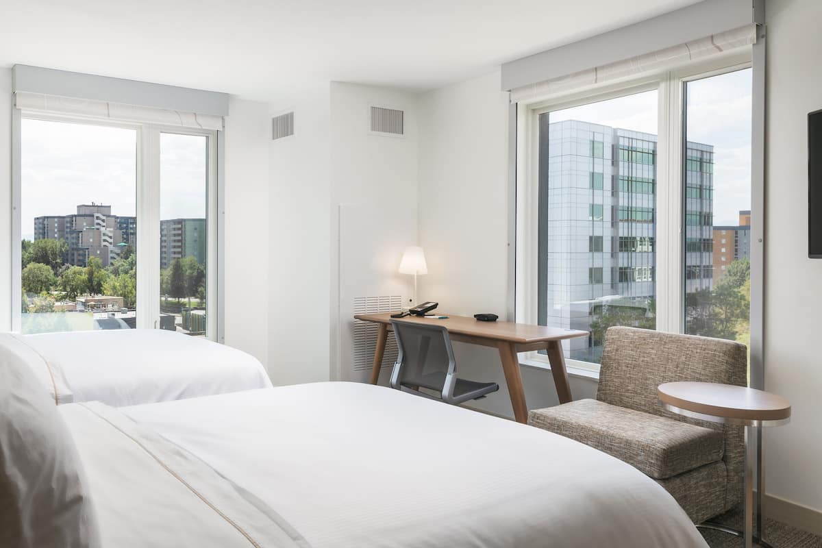 A hotel room with two beds, a desk, a chair, and a small table.