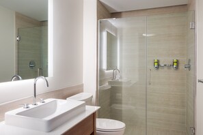 Een moderne badkamer met een douchecabine van glas, een witte wastafel en een toilet.