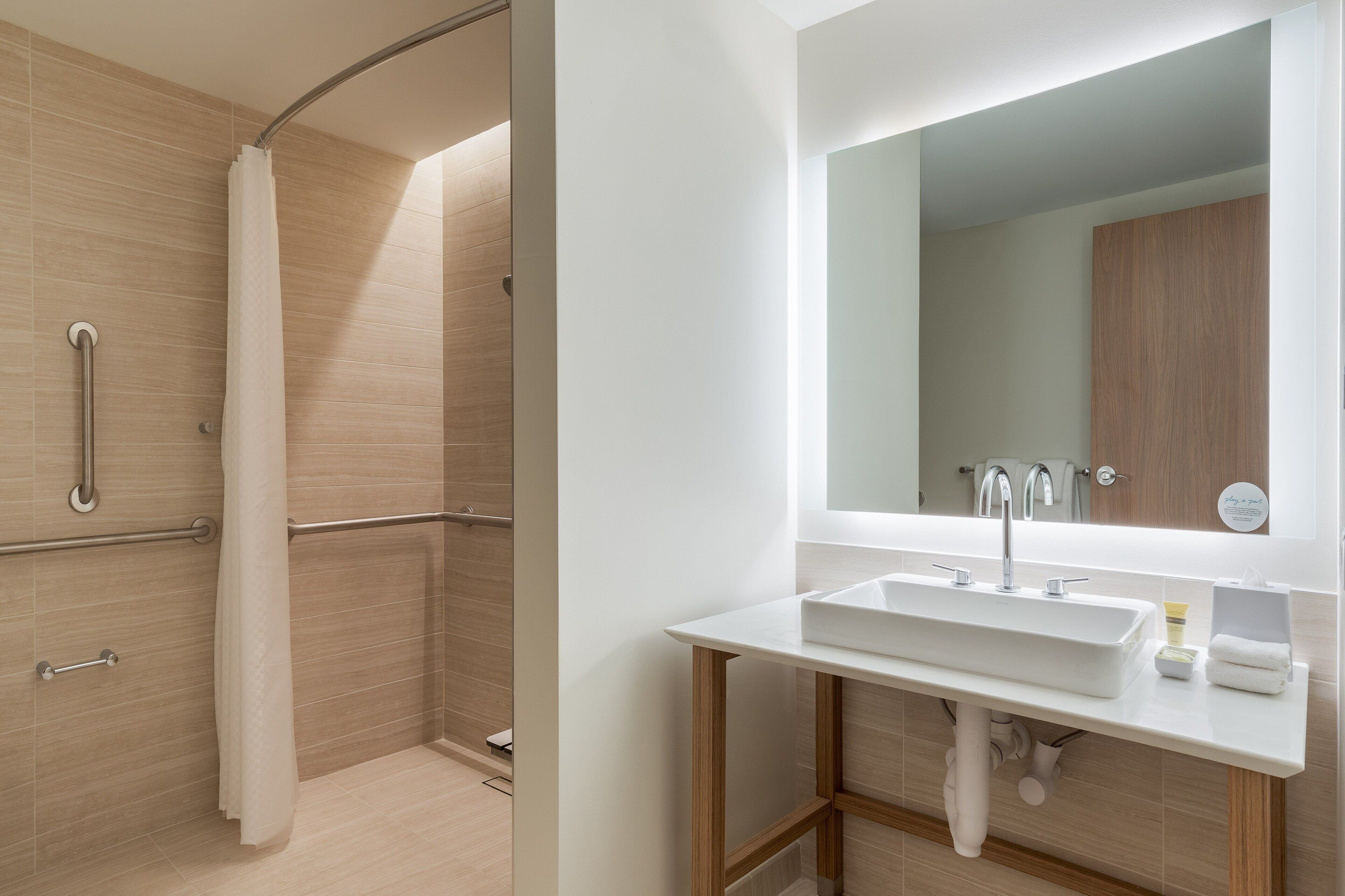 A modern bathroom with a shower, grab bars, a sink, and a mirror.