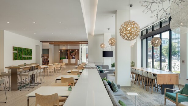 Un comedor moderno con largas mesas comunes, sillas y una barra alargada.