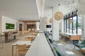 Un'area pranzo moderna con lunghe tavolate condivise, sedie e un bancone.