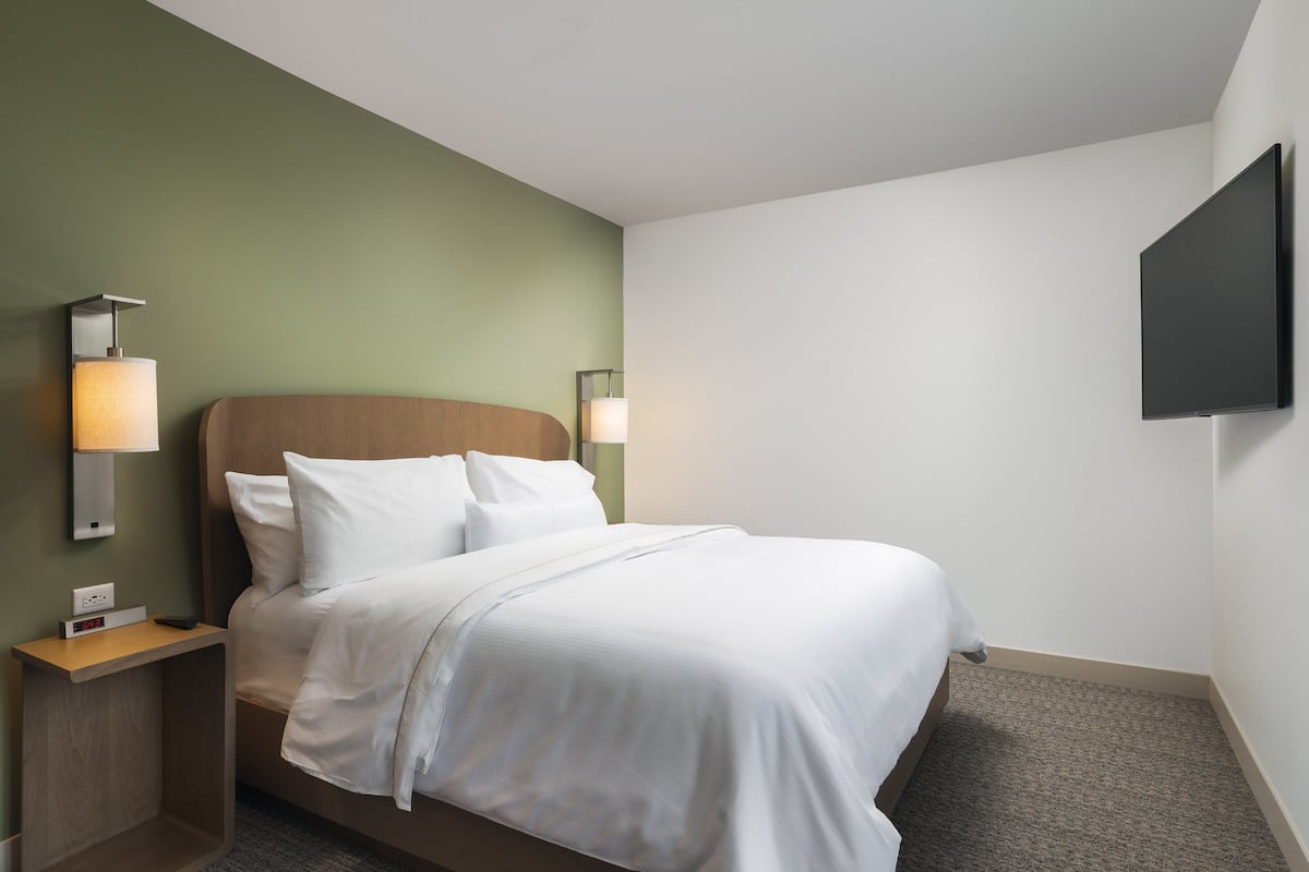 A neatly made bed with white linens, a wooden headboard, and two bedside lamps.