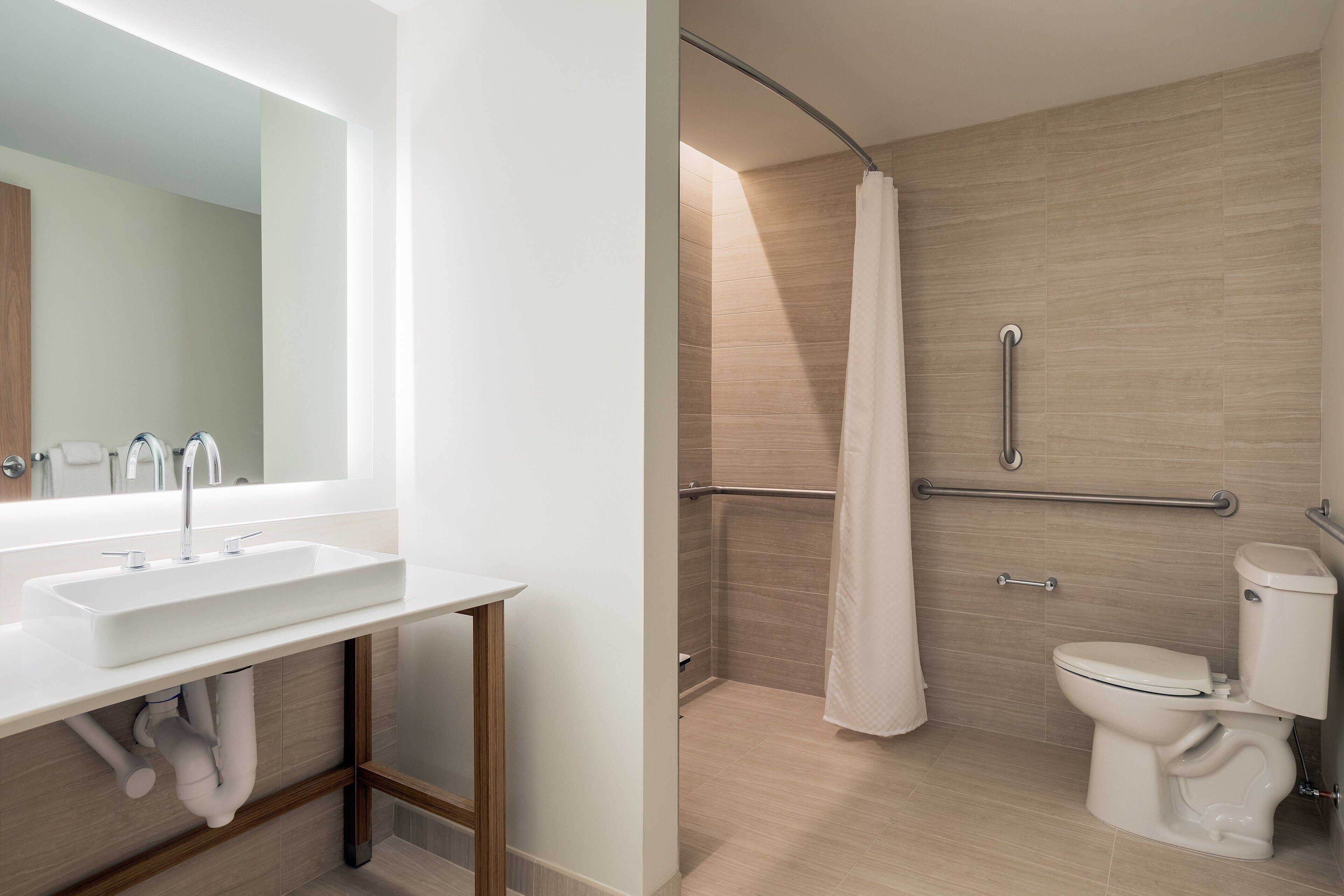 A modern bathroom with a sink, mirror, shower, and toilet.
